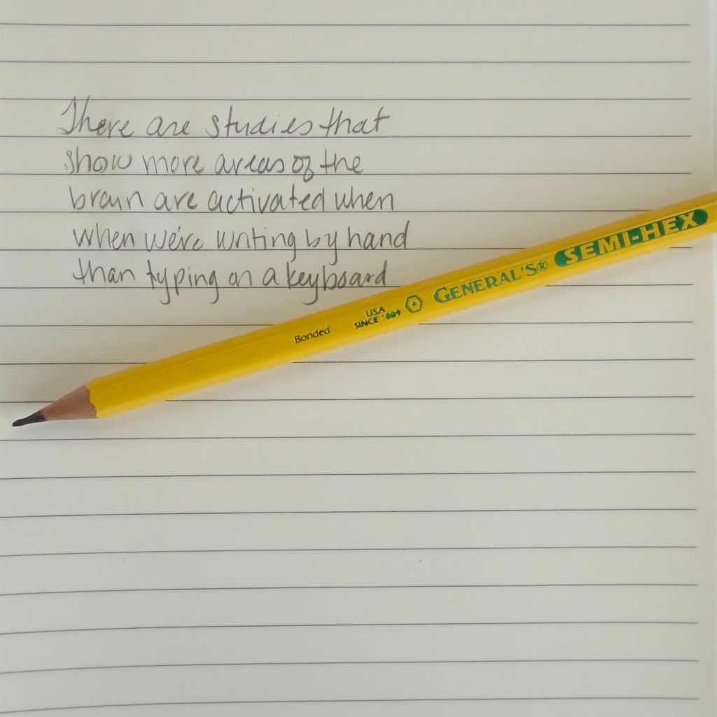 A General's® Semi-Hex Pencil in yellow rests on a lined notebook with handwritten notes about studies showing more brain areas are activated by writing by hand than typing.