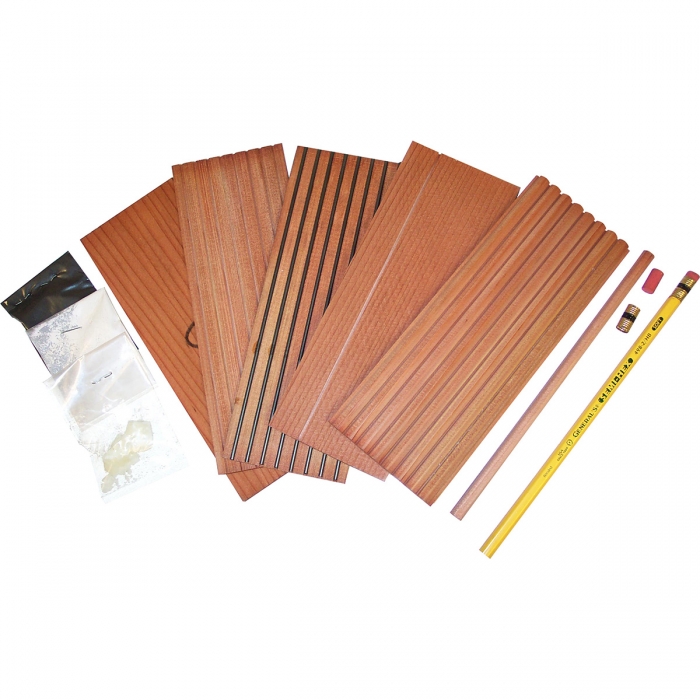 A collection of cedar wood slats, two pencils, two erasers, and clay, graphite, and wax packets displayed on a white background. The cedar wood slats have various grooves and textures.