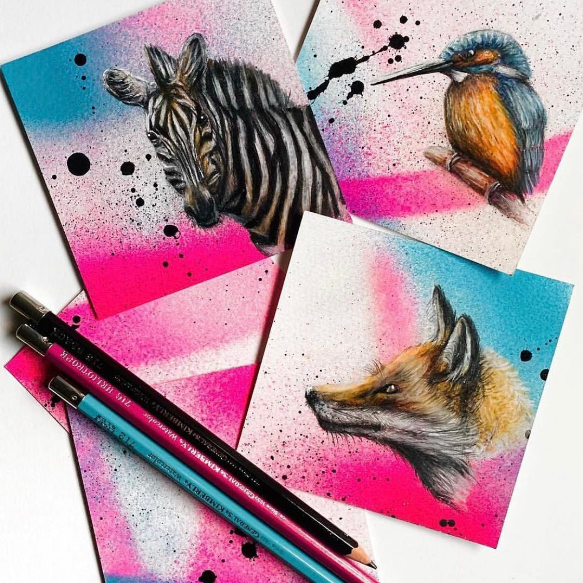 Three pieces of mixed media artwork by artist Jonathan Martinez with Kimberly® Watercolor Pencils and spray paint. Drawing in upper left corner: black and white zebra over an abstract blue, hot pink, and black spray painted background. Drawing in upper right corner: blue and yellow bird over a hot pink abstract spray painted background with an accent of blue and black drips. Drawing in bottom right corner: tan, black, and white fox over a hot pink and blue abstract spray painted background with drops of black spray paint. Bottom left corner: Black, Heliotrope, and Light Blue Kimberly® watercolor pencils resting on a hot pink abstract spray painted background.