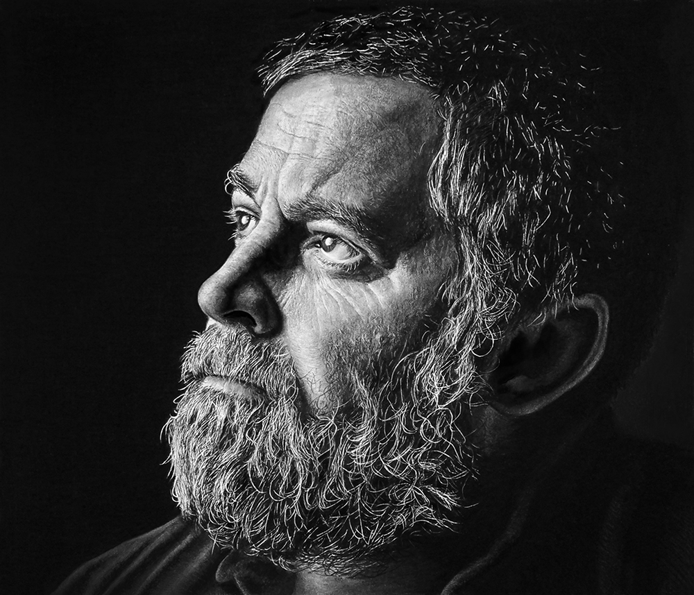 Black and white portrait of an older man with a bushy beard, looking thoughtfully upward. The lighting highlights the textures of his hair, beard, and facial features, creating a dramatic, contemplative mood.